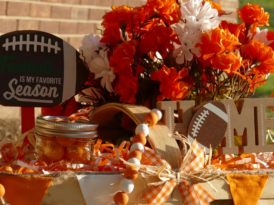 Orange and white game-day basket with bright orange florals, a wood HOME sign, gingham bow, and painted bead garland.